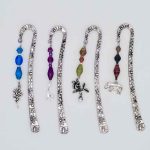 Photo of metal bookmarks available for purchase. This set shows 4 different stamped metal bookmarks with a beaded hanging dangle in various colors with a variety of different shaped charm choices for the bottom. Choose 1 charm per bookmark.