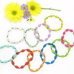 Bright spring summer color grouping of beaded stretch bracelets. There are 2 bright yellow flowers above the bracelets. There are 10 bracelets in a variety of bright colors including greens, reds, pinks, blue, orange, yellow, lavender & white.