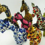 Photo of 7 mini stuffed animal giraffes available to purchase. The giraffes come in a variety of different colors/patterns of African kitenge cloth.