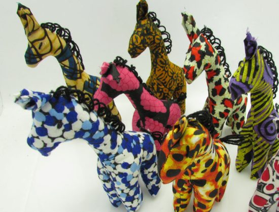 Photo of 7 mini stuffed animal giraffes available to purchase. The giraffes come in a variety of different colors/patterns of African kitenge cloth.