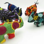 Photo of 7 mini stuffed animal rhinos available to purchase. The rhinos come in a variety of different colors/patterns of African kitenge cloth.