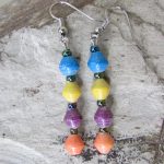 One pair of 4 bead multi-color bead earrings on small hook laying on a quartz-like surface in swirling gray on white. Each earring contains 4 small round beads in 4 different colors. Handmade by Ugandan women artisans from recycled paper.