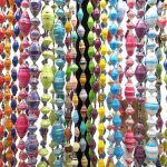 Closeup photo of many of Outreach Uganda's colorful paper bead necklaces hanging straight down from a black jewelry rack so you can see their beautiful colors and patterns. These necklaces are handcrafted by Ugandan women out of paper.