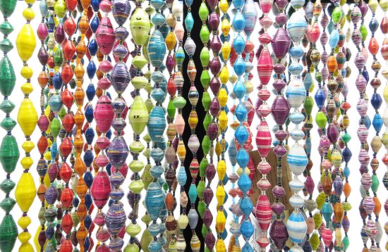 Closeup photo of many of Outreach Uganda's colorful paper bead necklaces hanging straight down from a black jewelry rack so you can see their beautiful colors and patterns. These necklaces are handcrafted by Ugandan women out of paper.