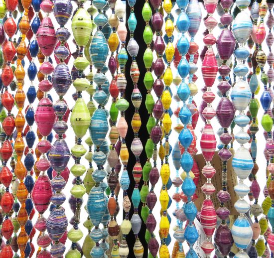 Closeup photo of many of Outreach Uganda's colorful paper bead necklaces hanging straight down from a black jewelry rack so you can see their beautiful colors and patterns. These necklaces are handcrafted by Ugandan women out of paper.