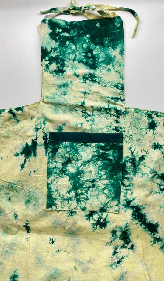 Photo of adult size apron in a yellow/green tie dye pattern on a dark background that is available to purchase. The apron has a front center pocket and bib type top with neck and waist tie straps.