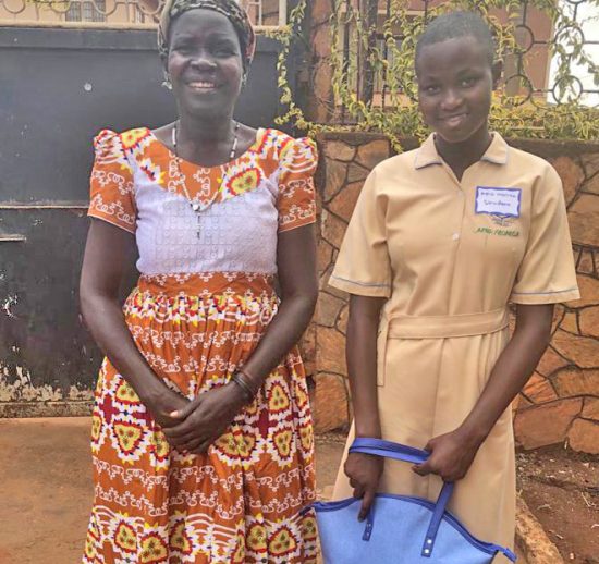 Secondary student in Jinja, in school uniform, standing with her smiling mother, and holding a gift from her sponsor in the U.S.